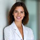 Portrait d'une dermatologue femme souriante et rassurante, portant une blouse blanche, symbolisant la confiance et l'expertise médicale.